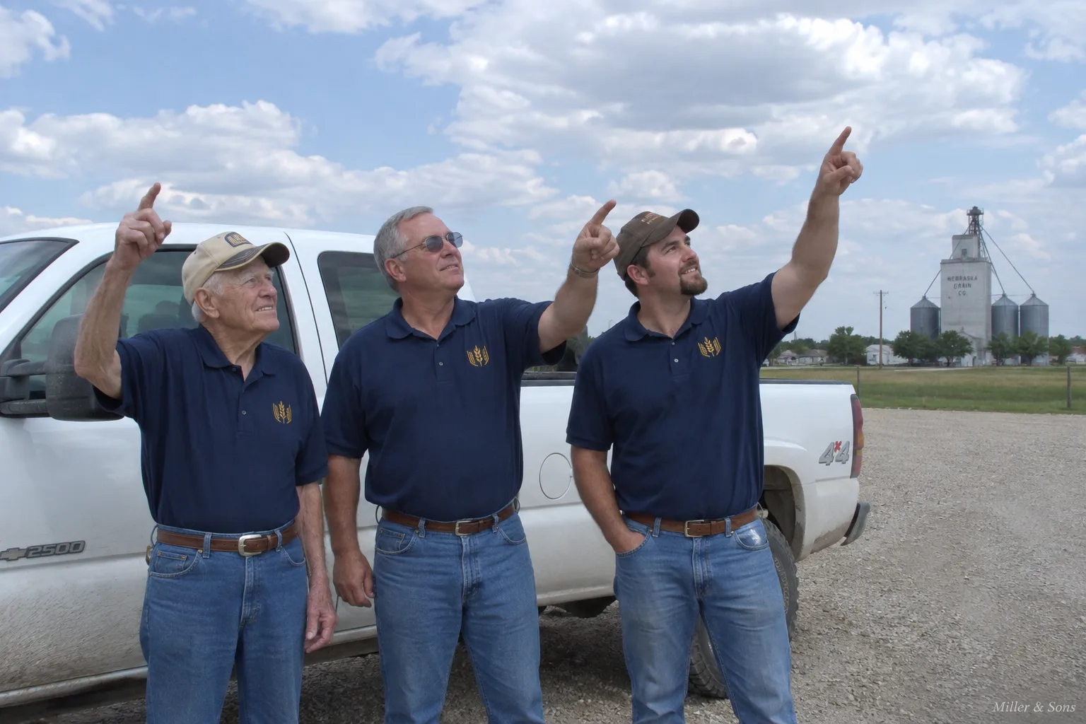 Three generations of Millers pointing at the sky in front of a company truck